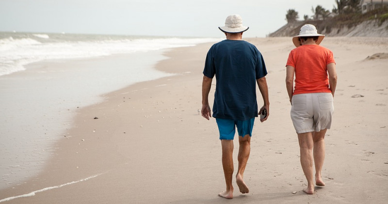 Dos personas mayores de espaldas caminando por una playa