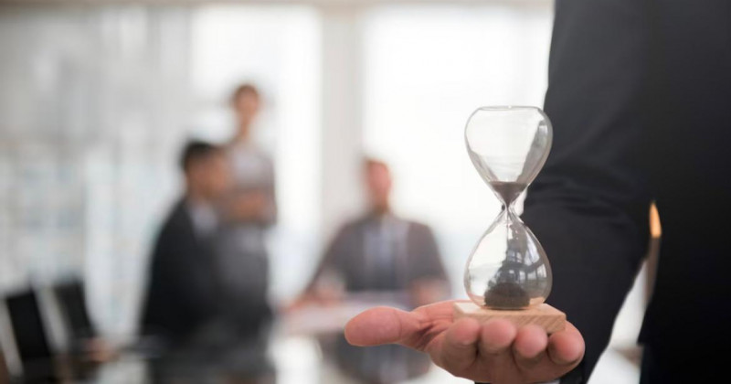 Gestor sostiene un reloj de arena, sala de reuniones al fondo